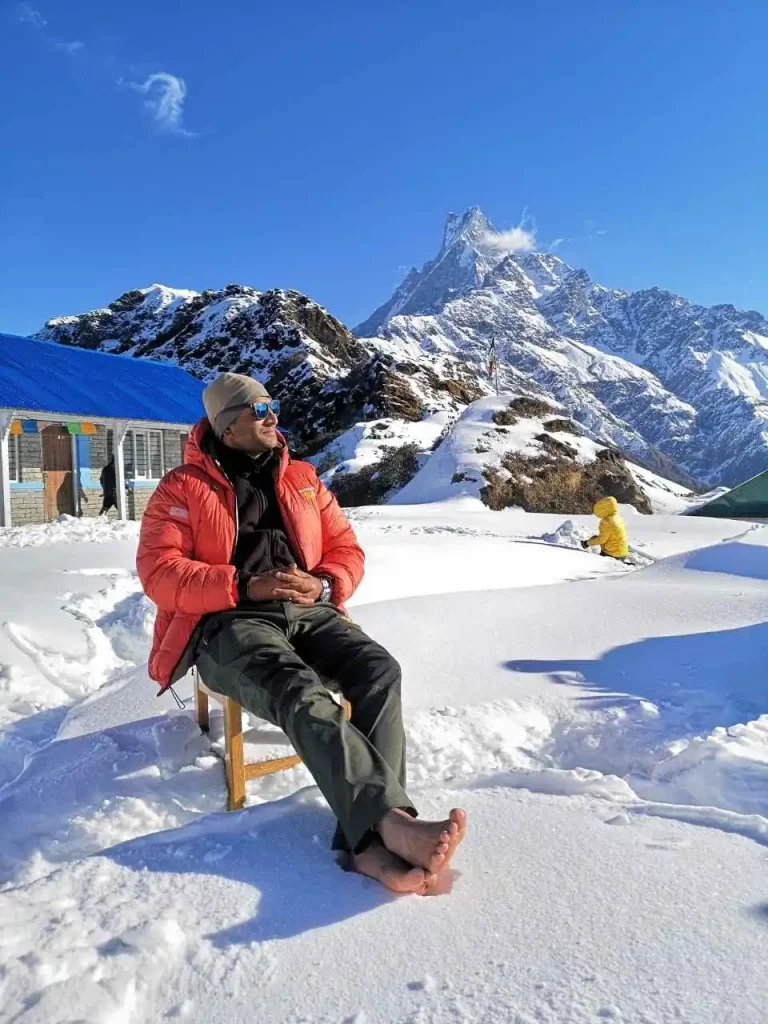 Saligram sitting barefoot in the snow at Mardi Himal High Camp with Machhapuchhre in the background
