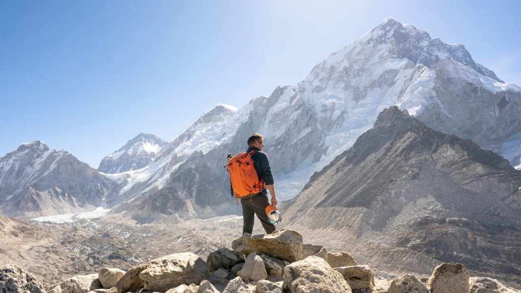 Everest Base Camp Trek Solo trekker standing on a rocky ridge overlooking snow-capped Himalayan peaks