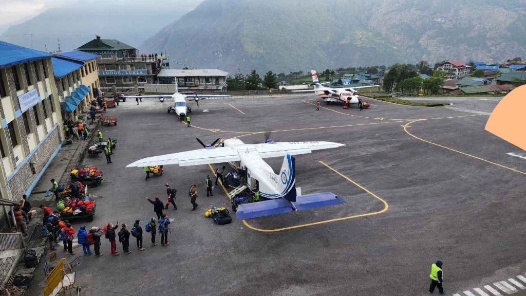 Lukla flight and airport guide – trekkers and porters queue with luggage beside a plane at Tenzing-Hillary Airport